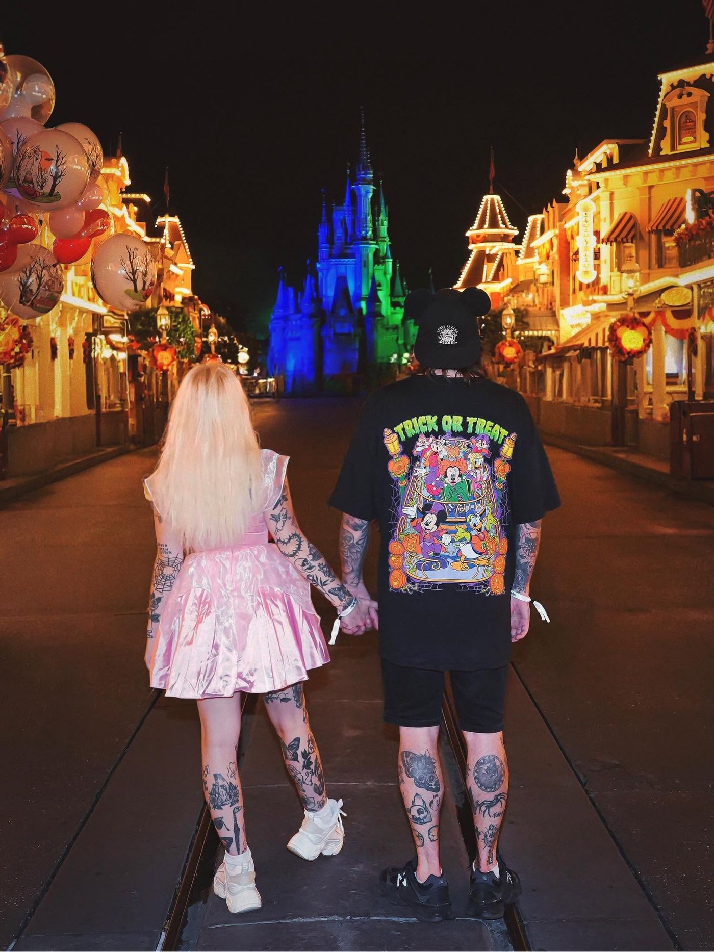 A couple walking hand in hand down Main Street at night towards the castle, wearing Mouse House