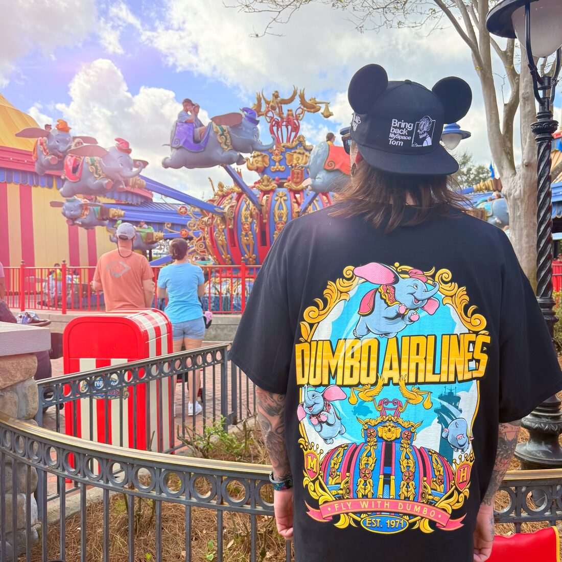 The back of a black Mouse House tee worn at a theme park, the design printed large across the back