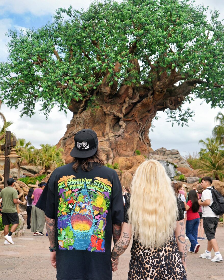Two people in matching Mouse House Clothing tees at a theme park, seen from behind
